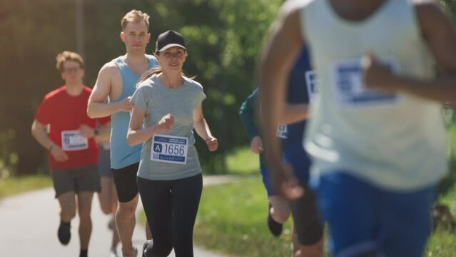 Slow Motion Portrait of a Woman Running and Participating in a Marathon in a Park. Strong Athletic Female Jogger Racing Other Runners with Determination for the First Place in the Finish Line