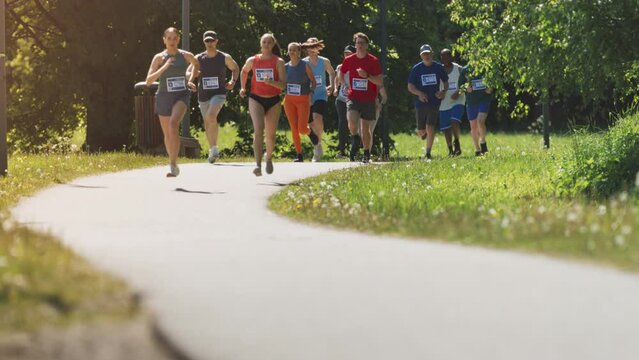 Ground Level Shot of Resolute Diverse Group of People Running on a City Marathon Event Through a Green Park Trail. Joggers Participating in a Race, Relentlessly Trying to Reach the Finish Line