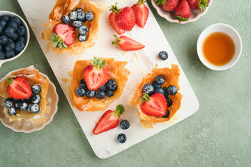 Phyllo or filo pies with fresh berries strawberries and blueberries, cheese filling topped with fresh mint on white plate. Homemade Filo pastry paskets. Delicious filo pastry dessert.