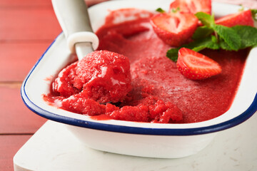 Strawberry granita or fresh berry sorbet in white rustic bowl on old wooden table background. Ice cream with strawberry and mint. Summer treat. Top view.