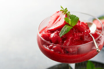 Strawberry granita or fresh berry sorbet in glass on old  grey table background. Texture of ice cream or sorbet. Ice cream with strawberry and mint. Sorbet recipe. Summer treat. Selective focus. - obrazy, fototapety, plakaty