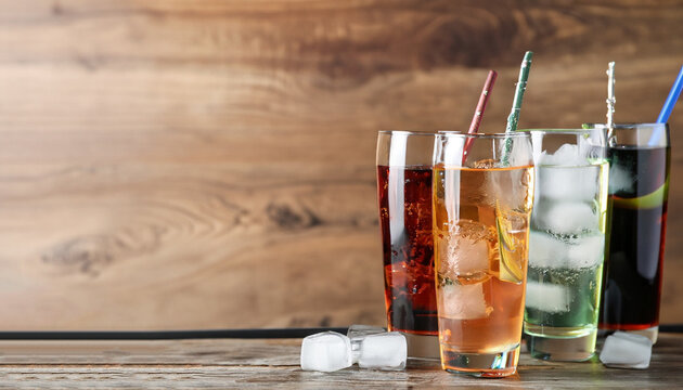 Glasses of different refreshing soda water with ice cubes on wooden table. Space for text