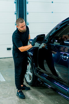 Focused Male car wash worker in black gloves polishes the mirror of a luxury blue car using a polishing sponge car care concept 