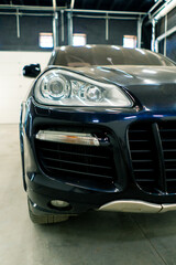Car wash close-up of the front headlight bumper and grille of a black luxury car after detailing at a parking lot or car service center 