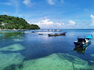 Banda Island, Indonesia - May 20, 2022. Beautiful sea and beach view with turquoise sea color, white clouds, blue sky, trees and bright sunshine and sailing ships.