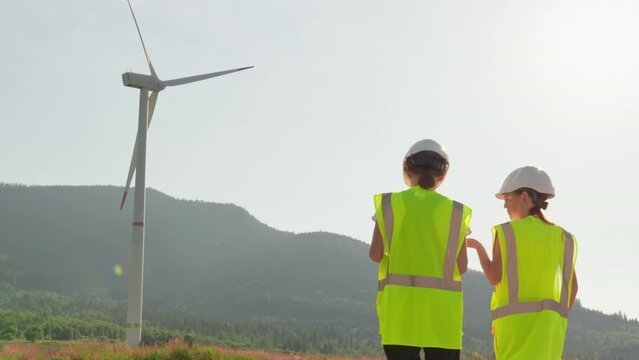 End of the working day. Two engineer workers are leaving the wind farm. People near a large windmill, electric generator. Women chat and discuss working moments and a wind turbine.