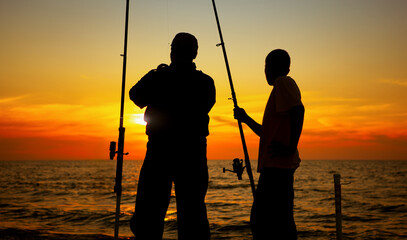 A silhouette of two men fishing