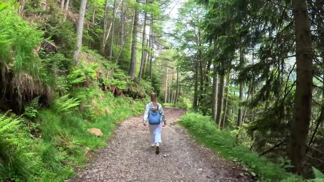 Woman walks on dirt road through mountain woods