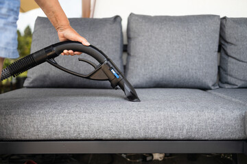 Cleaning service company employee removing dirt from furniture in flat with professional equipment. Female housekeeper arm cleaning sofa with washing vacuum cleaner close up. High quality photo
