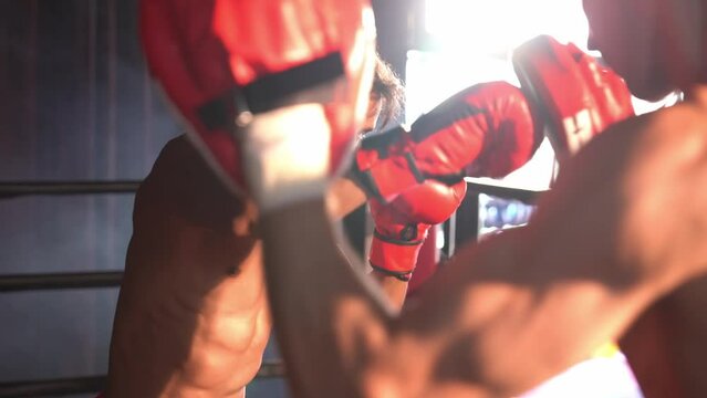 Asian and Caucasian Muay Thai boxer unleash punch in fierce boxing training session, delivering punching strike to sparring trainer, showcasing Muay Thai boxing technique and skill. Impetus