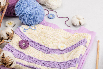 Fototapeta na wymiar Handmade crocheted baby t-shirt in lilac tones. Stuff contains thread, hooks, knitting needles