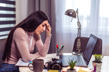 Young frustrated woman working at office desk suffering from chronic daily headaches
