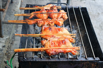 Chicken in bamboo clamp roasting on retro charcoal stove, street foof in Thailand.