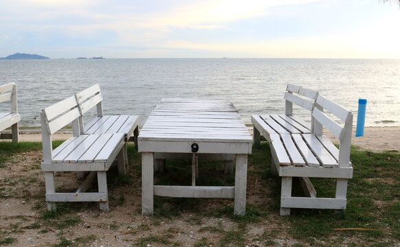 Set white painted table and benches on sand and sea, sky background with sunlight, white cloud in sky.
