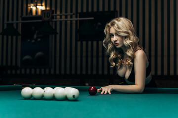 Blond woman playing enjoying billiard, hold cue hit white billiard balls on table with green...