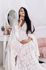 Vertical image pregnant woman strokes hugging the belly tummy abdomen enjoying pregnancy. Future family, baby infant expecting child inside, lady in white dress in bedroom modern interior
