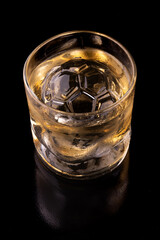 soccer ball shaped clear ice in whiskey glass isolated on black background