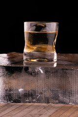 single malt whiskey on the rocks with clear ice in sphere isolated on wooden table over block of ice
