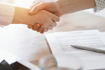 Fototapeta na wymiar Business people shaking hands above contract papers just signed on the wooden table, close up. Lawyers at meeting. Teamwork, partnership, success concept