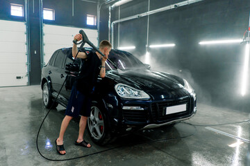 Fototapeta na wymiar A male car wash employee washes a black luxury car with a high-pressure washer in the car wash bay 