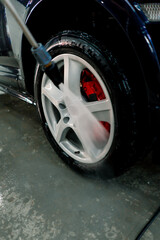 Close-up of a male car wash employee washing the rim and tire of a black luxury car using a high-pressure washer 