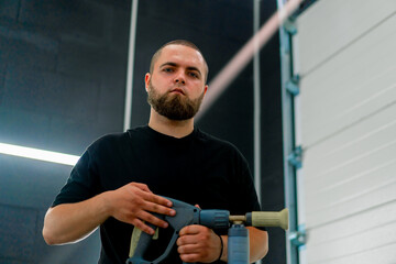 Portrait of a serious man with a beard of a car wash worker who holds a foam generator nozzle in his hands car care concept 