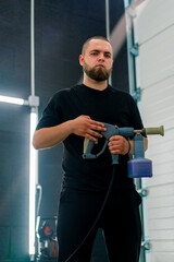 Portrait of a serious man with a beard of a car wash worker who holds a foam generator nozzle in his hands car care concept 