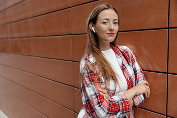 Elegant young caucasian woman listening to music using headphones and smartphone outdoors. Brunette wears casual clothes. Technological device concept.