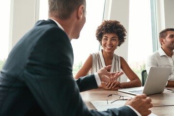 Multicultural team. Young and beautiful afro american woman discussing something with colleagues and smiling while sitting in the modern office