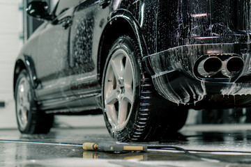 Fototapeta premium Close-up of car foam application on the rear tire of a black luxury car in the car wash box of the car care concept