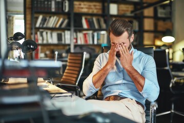 Hard work. Young exhausted bearded businessman covering his eyes and feeling stressed while sitting in modern office