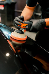 Close-up of a car wash worker using a polishing machine to polish the hood of a black luxury car 