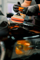Close-up of a car wash worker using a polishing machine to polish the hood of a black luxury car 