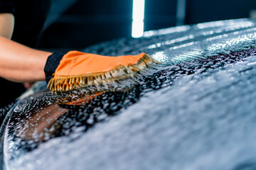 Close-up of a car wash worker using a microfiber cloth to wash a black luxury car with car wash...