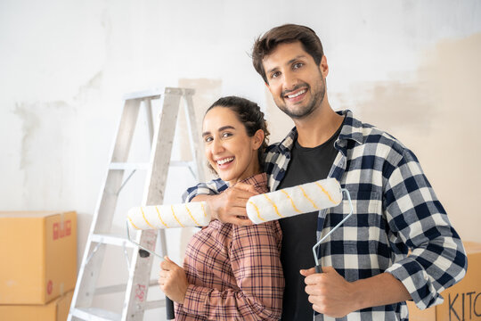 Happy Brazilian couple holding roller in hand and looking to camera at new home location. Home renovation DIY renew home concept. 