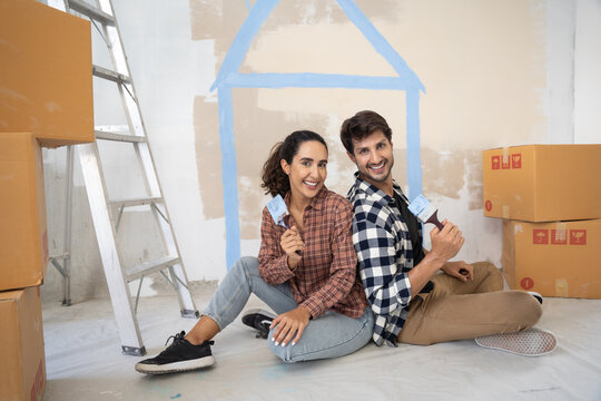 Young latin couple looking to camera and smiling together. They painting new home together.New home concept.