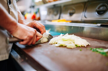 Chefs man hands chopping onion on wooden board in kitchen