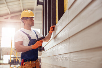Handsome young man builder installing exterior wood siding