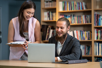 Beautiful woman talking with business man at library. They doing extracurricular work preparing report from university to get highest exam score sits at table with laptop in home office