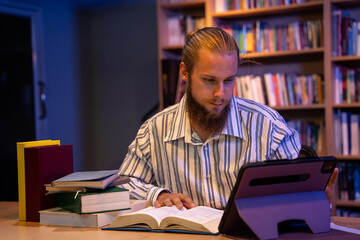 Male teacher working in library in night time. He using tablet to searching data in library alone.