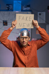 Strange man in a protective foil cap and glasses holding banner with fake news message. Conspiracy...