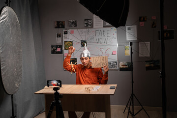 Strange young man in tinfoil hat recording video or live streaming using phone in home studio. Fake news conspiracy theories