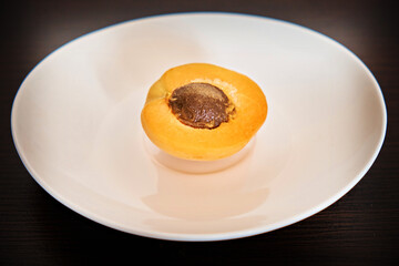Half of an apricot with a stone lies on a white plate on a dark background. Close-up