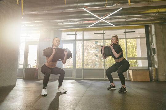 Group of athletic women In aerobics class performing bag squat exercise in gym