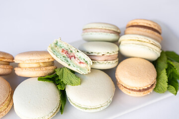 Macaroons of different colors with sprigs of mint on a white background.