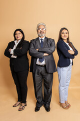 Group of positive indian business people wearing suit standing with their arms crossed isolated on beige studio background. Senior and young corporate man and women.