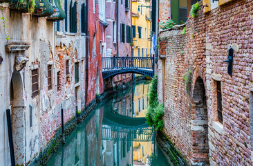 Narrow water canal and red brick worn out buildings built on water in Venice, Italy.
