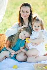 Beautiful young mother with little daughters on a picnic in the field. Summer breakfast with lemons. Family.