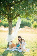 Beautiful young mother with little daughters on a picnic in the field. Summer breakfast with...