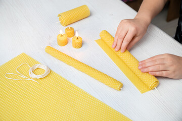 Kid making natural rolled beeswax candle from pressed beeswax honeycomb sheet at home indoors....